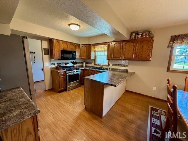 9910 Quachita Ct, Fort Wayne, IN 46804 - kitchen featuring appliances with stainless steel finishes, a peninsula, brown cabinets, light wood-style flooring, and a textured ceiling