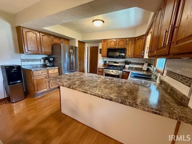 9910 Quachita Ct, Fort Wayne, IN 46804 - kitchen featuring stainless steel appliances, light wood finished floors, tasteful backsplash, a peninsula, and brown cabinetry