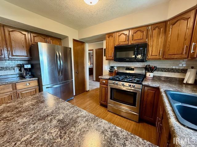 9910 Quachita Ct, Fort Wayne, IN 46804 - kitchen with stainless steel appliances, light wood finished floors, brown cabinets, decorative backsplash, and a textured ceiling