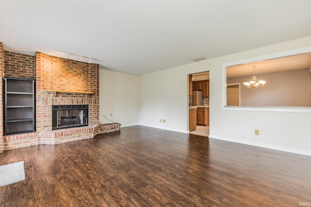 4301 W Friar Dr, Muncie, IN 47304 - unfurnished living room with a chandelier, wood finished floors, a brick fireplace, and rail lighting