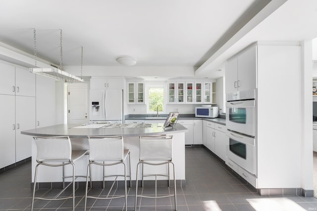 1144 N Warwick Rd, Muncie, IN 47304 - kitchen featuring white appliances, white cabinetry, glass insert cabinets, and a kitchen bar
