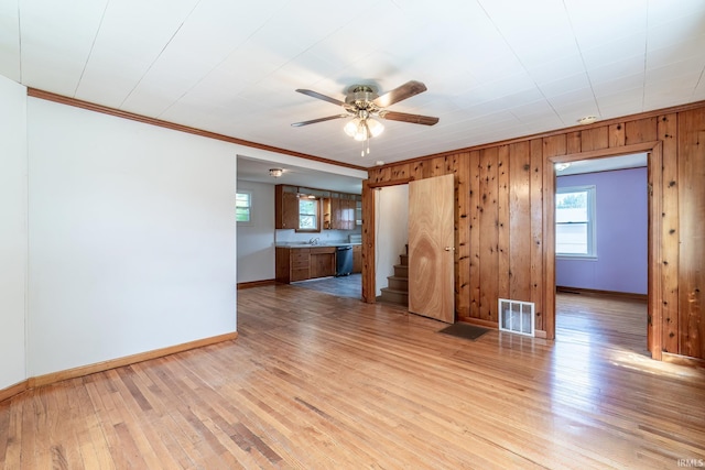 208 Chestnut St, Avilla, IN 46710 - unfurnished living room featuring ceiling fan, ornamental molding, stairs, light wood-style floors, and wood walls