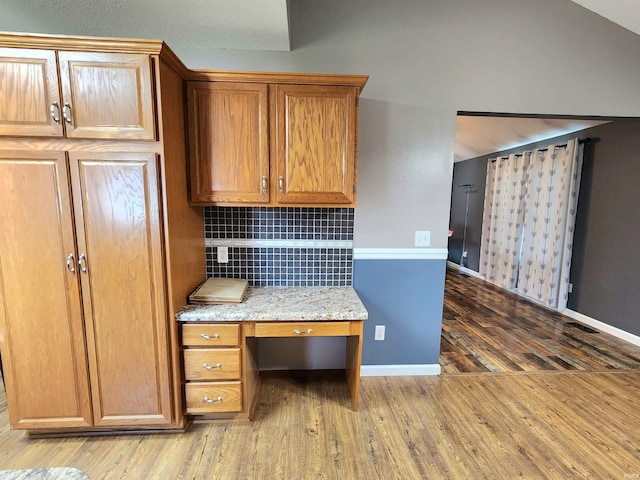 9421 Mill Ridge Run, Fort Wayne, IN 46835 - kitchen featuring built in study area, wood finished floors, backsplash, brown cabinets, and light stone countertops