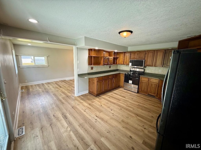 1228 N Main St, Kewanna, IN 46939 - kitchen featuring appliances with stainless steel finishes, brown cabinets, open shelves, light wood finished floors, and a textured ceiling