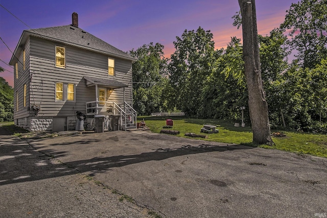 817 Middlebury St, Elkhart, IN 46516 - back of house at dusk featuring a chimney, a yard, and asphalt driveway