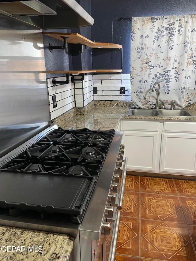 kitchen featuring stone counters, sink, backsplash, stainless steel range with gas stovetop, and white cabinets