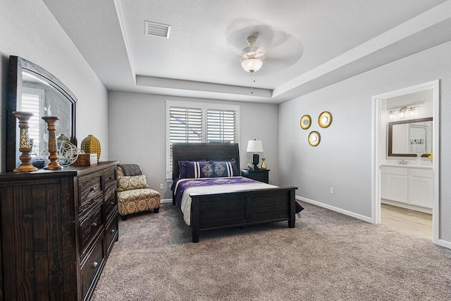 bedroom with carpet floors, a tray ceiling, ceiling fan, and connected bathroom