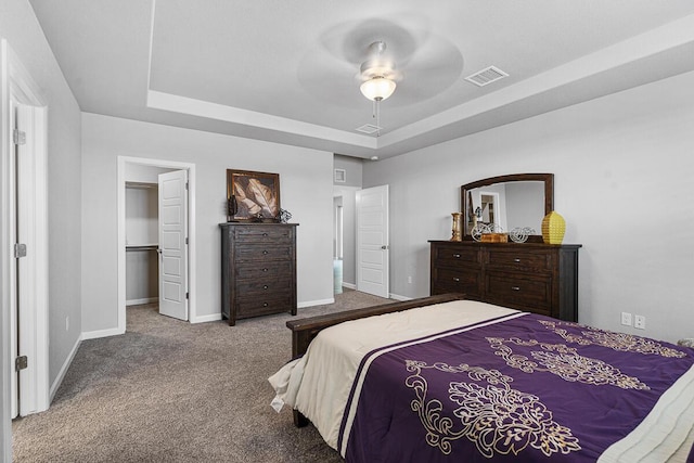 carpeted bedroom with a raised ceiling, ceiling fan, a closet, and a spacious closet