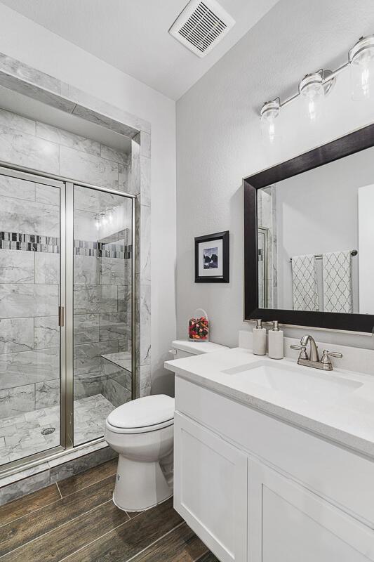 bathroom with hardwood / wood-style flooring, toilet, an enclosed shower, and vanity