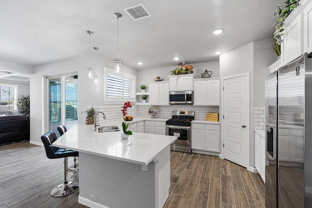 kitchen featuring hanging light fixtures, sink, appliances with stainless steel finishes, a kitchen bar, and white cabinetry