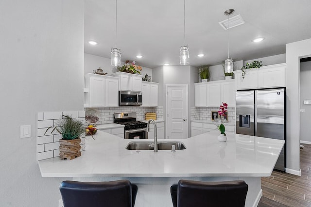 kitchen featuring kitchen peninsula, appliances with stainless steel finishes, dark wood-type flooring, sink, and hanging light fixtures