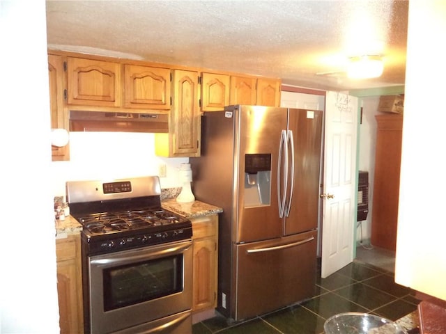 kitchen with stainless steel appliances, light stone counters, dark tile flooring, and a textured ceiling