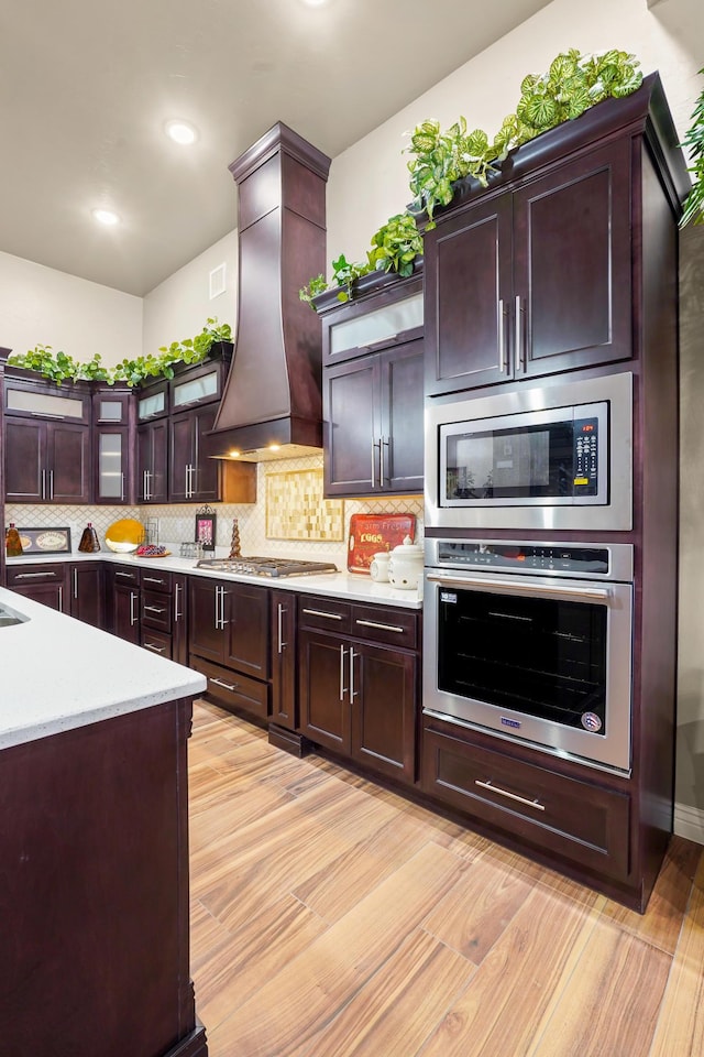 2425 Cesar Cordova Pl, El Paso, TX 79938 - kitchen featuring dark brown cabinets, light hardwood / wood-style floors, stainless steel appliances, premium range hood, and tasteful backsplash
