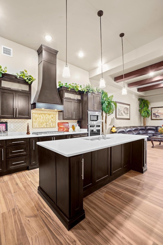 2425 Cesar Cordova Pl, El Paso, TX 79938 - kitchen featuring hanging light fixtures, light hardwood / wood-style flooring, custom range hood, backsplash, and dark brown cabinetry