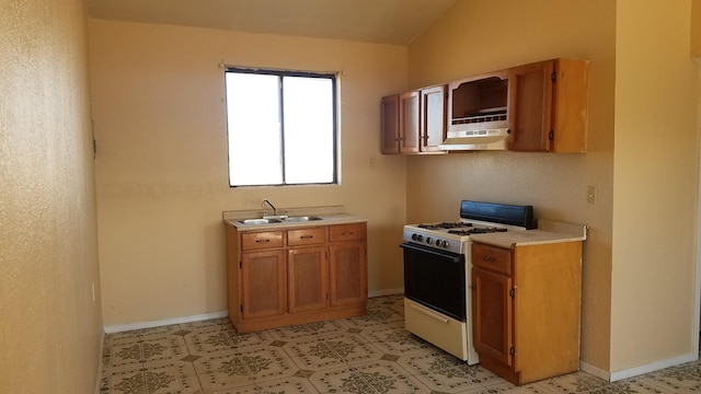 kitchen with white gas range oven, sink, light tile floors, and lofted ceiling