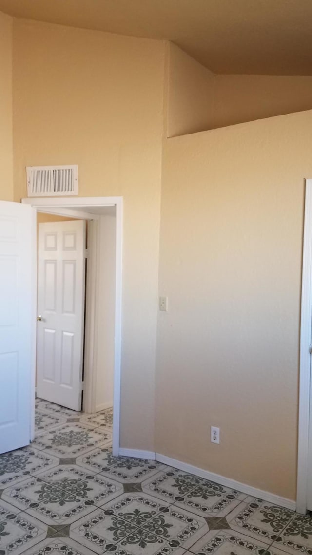 tiled empty room featuring lofted ceiling