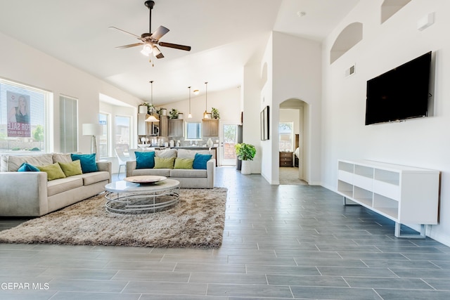 living room with visible vents, baseboards, arched walkways, high vaulted ceiling, and a ceiling fan