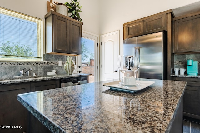 kitchen featuring a sink, stainless steel appliances, dark stone counters, dark brown cabinetry, and decorative backsplash