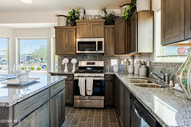 kitchen with tasteful backsplash, wood finish floors, light stone countertops, stainless steel appliances, and a sink