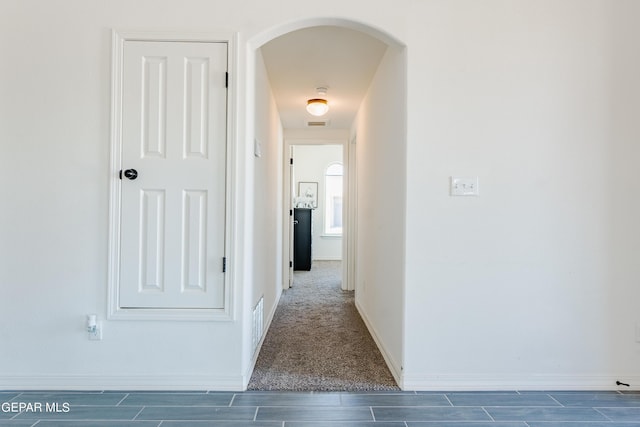 hall with visible vents, baseboards, and arched walkways