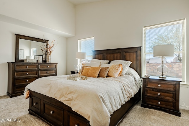 bedroom with baseboards, multiple windows, a high ceiling, and light carpet