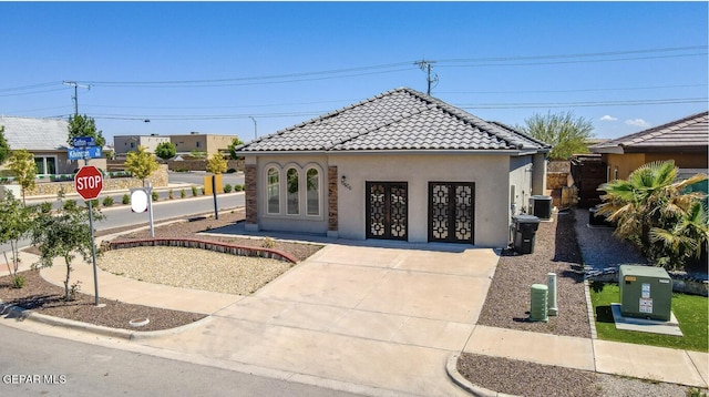view of front of house featuring a tiled roof, concrete driveway, central AC unit, stucco siding, and french doors