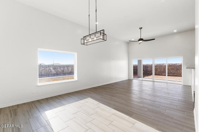 empty room featuring a high ceiling, ceiling fan with notable chandelier, and a healthy amount of sunlight