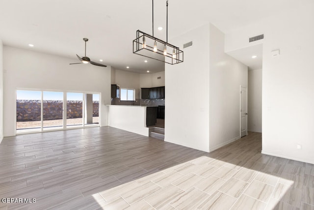 unfurnished living room featuring light hardwood / wood-style flooring, ceiling fan with notable chandelier, and a towering ceiling