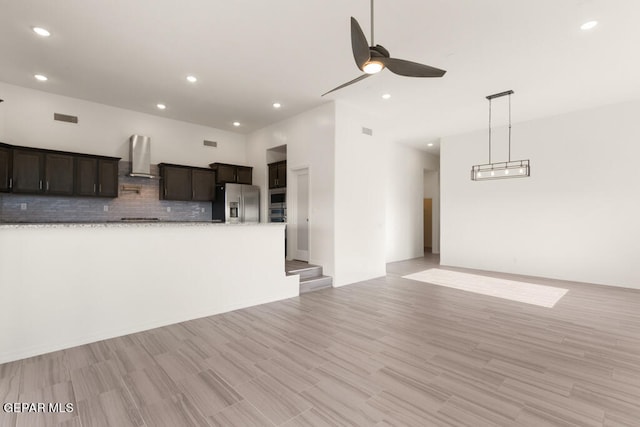 kitchen with light wood-type flooring, tasteful backsplash, wall chimney range hood, ceiling fan, and stainless steel fridge with ice dispenser