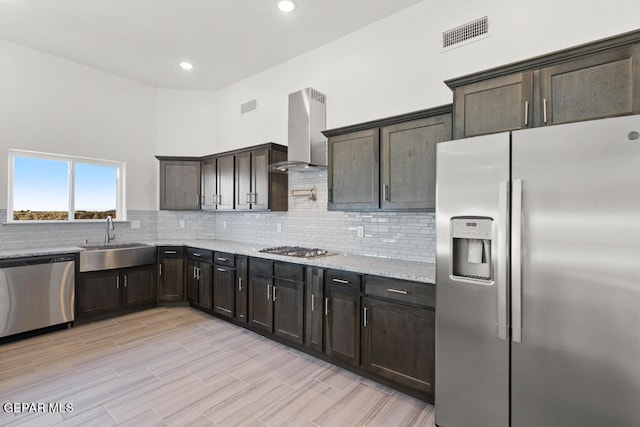 kitchen with appliances with stainless steel finishes, light stone counters, backsplash, wall chimney range hood, and sink