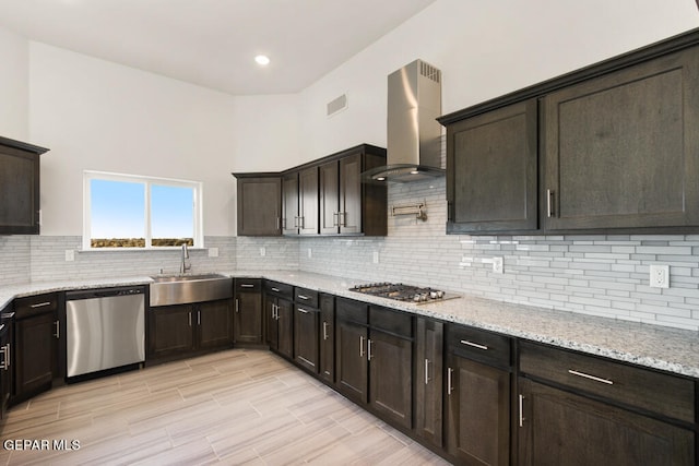 kitchen with light stone countertops, appliances with stainless steel finishes, sink, wall chimney range hood, and tasteful backsplash