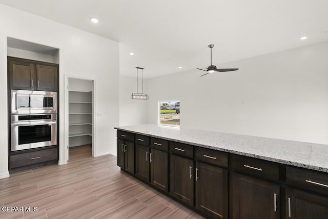 kitchen with appliances with stainless steel finishes, pendant lighting, ceiling fan, dark brown cabinets, and light stone countertops