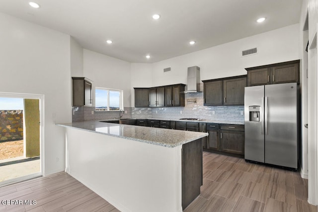 kitchen with wall chimney range hood, appliances with stainless steel finishes, light stone counters, and tasteful backsplash