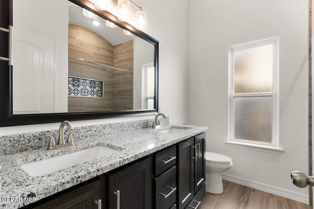 bathroom with hardwood / wood-style floors, vanity with extensive cabinet space, dual sinks, toilet, and a healthy amount of sunlight