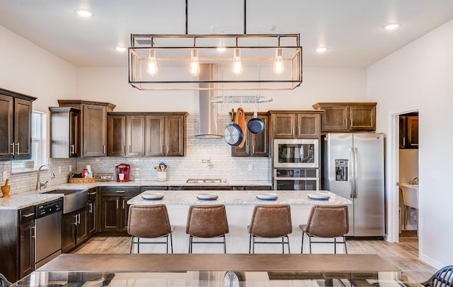 kitchen with a center island, light stone countertops, wall chimney exhaust hood, appliances with stainless steel finishes, and sink