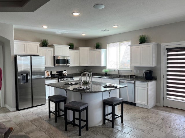 kitchen featuring a center island with sink, white cabinets, dark stone counters, and stainless steel appliances