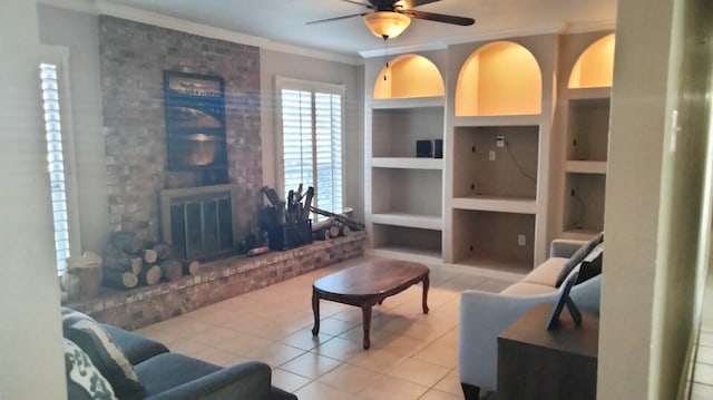 living room featuring ceiling fan, a brick fireplace, light tile floors, built in shelves, and crown molding