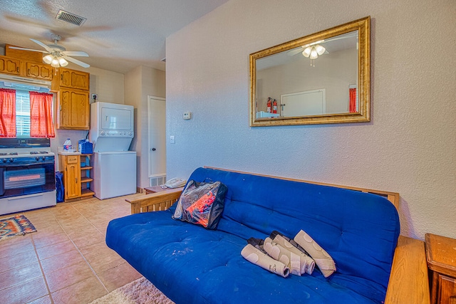 tiled living room featuring stacked washer / dryer and ceiling fan