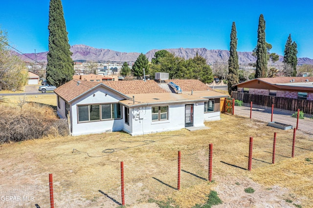 view of front of home featuring a front yard, cooling unit, fence, a shingled roof, and a mountain view