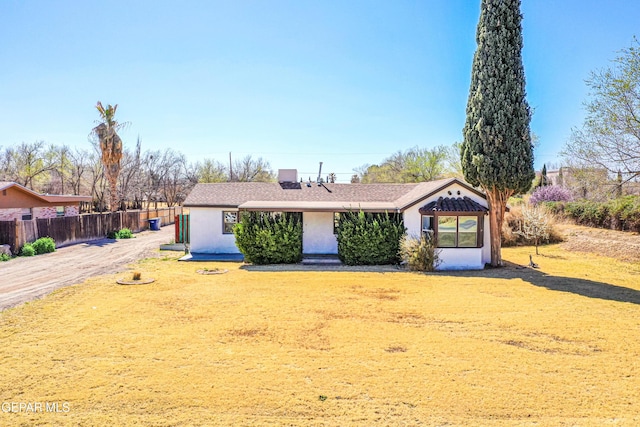 view of front facade featuring stucco siding, a front yard, and fence