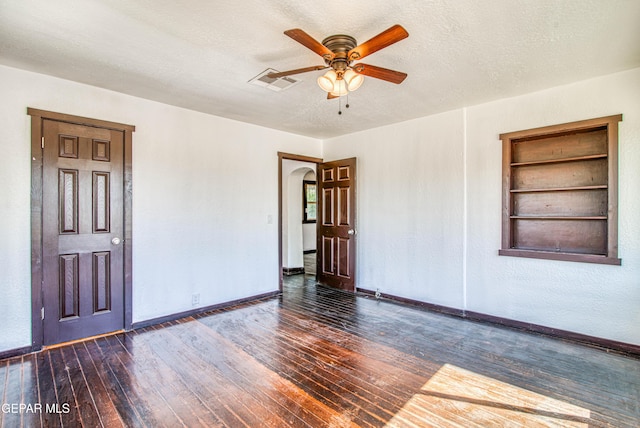 unfurnished room with hardwood / wood-style floors, built in features, visible vents, arched walkways, and a textured ceiling