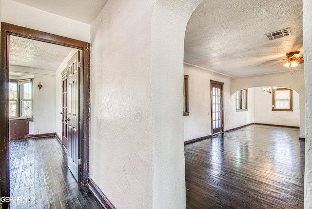 unfurnished room featuring visible vents, arched walkways, dark wood-type flooring, and a textured ceiling