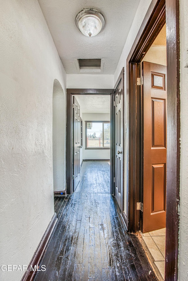 hall with a textured ceiling, attic access, a textured wall, and hardwood / wood-style floors