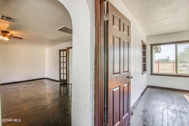 hallway with hardwood / wood-style floors, visible vents, arched walkways, and a textured ceiling