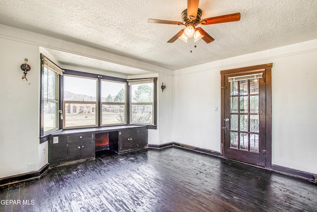 spare room with a textured ceiling, wood finished floors, built in desk, baseboards, and ceiling fan