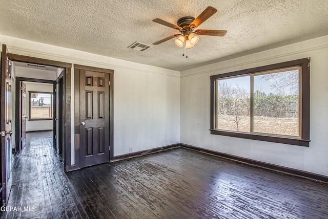 empty room featuring dark wood-style floors, visible vents, a ceiling fan, and baseboards