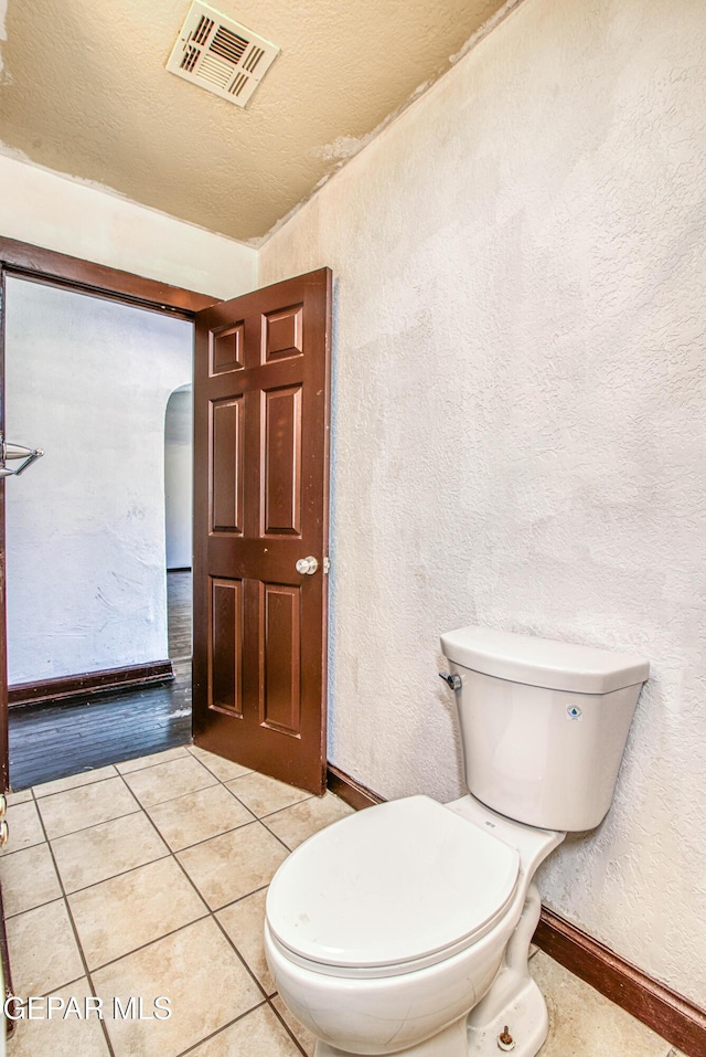 bathroom with visible vents, baseboards, tile patterned flooring, toilet, and a textured wall