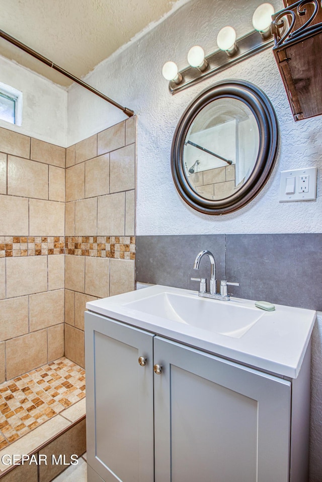 full bathroom featuring a tile shower, a textured ceiling, vanity, and a textured wall