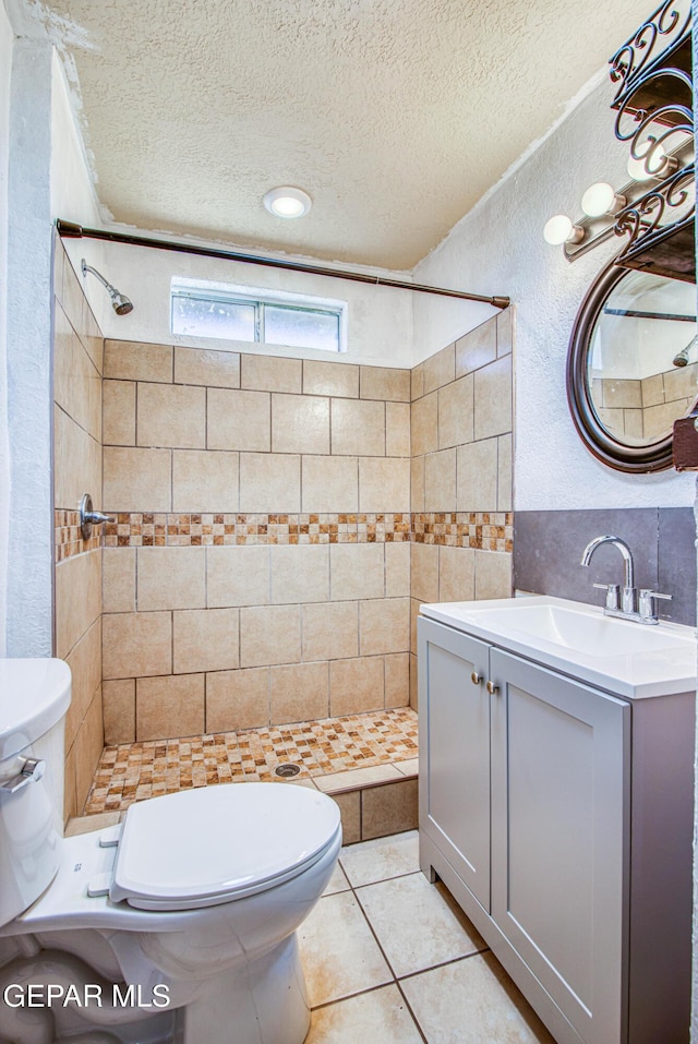 bathroom with tile patterned flooring, toilet, vanity, a tile shower, and a textured ceiling