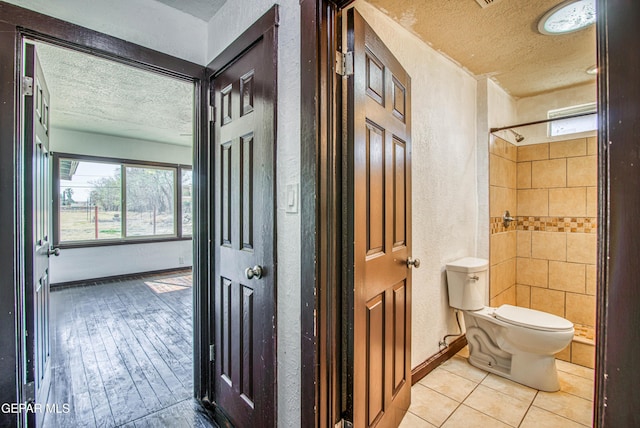 full bath featuring baseboards, toilet, tiled shower, a textured wall, and a textured ceiling